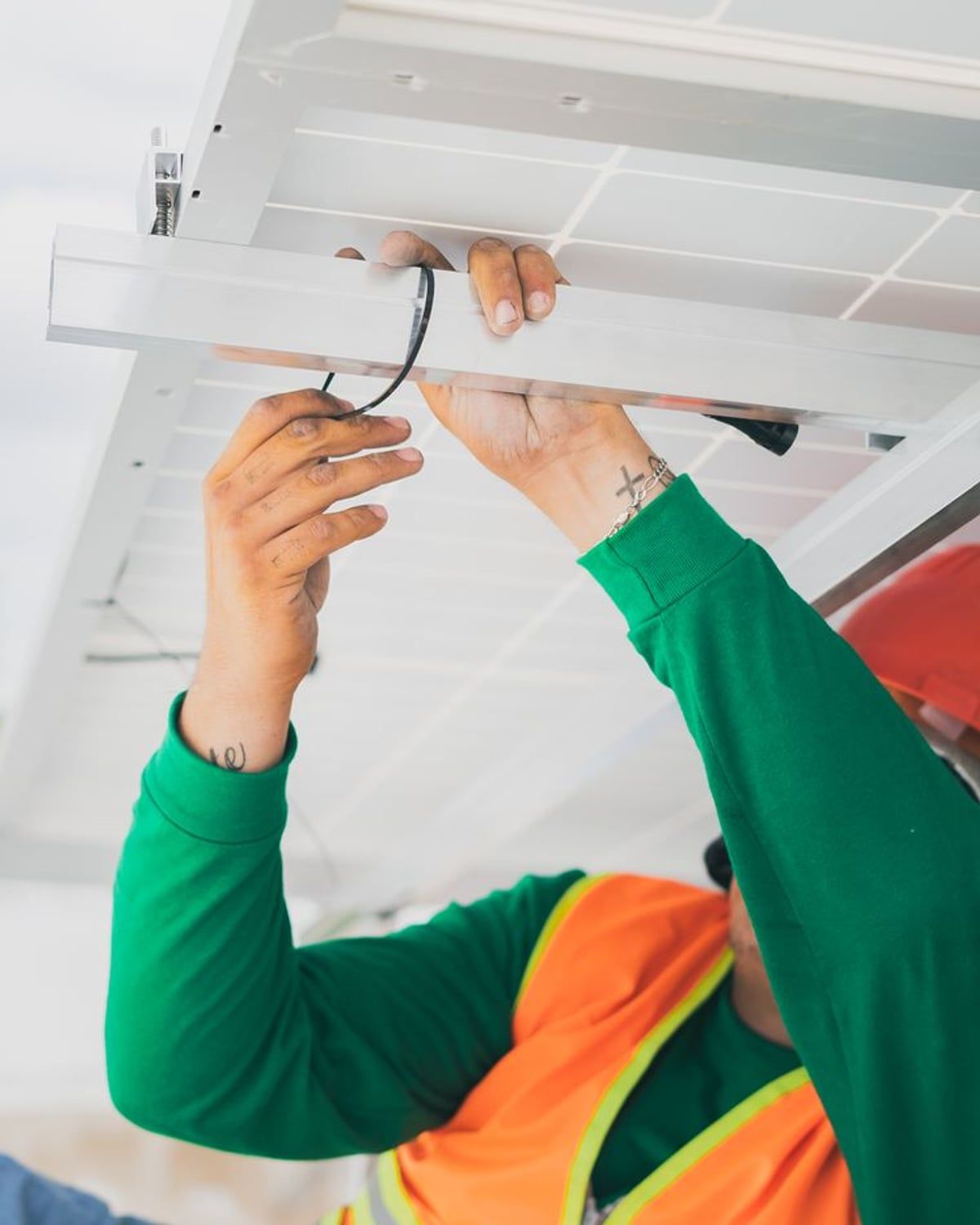 Montage einer Photovoltaik-Anlage — Monteur befestigt die Verkabelung unter einem Solarmodul